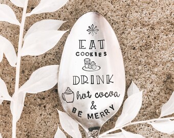 May include: A silver spoon with a black inscription that reads "Eat Cookies Drink Hot Cocoa & Be Merry".