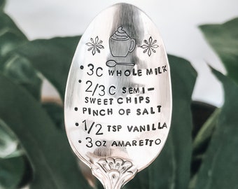 May include: A silver spoon with an engraved recipe for a hot chocolate drink. The recipe includes 3 cups of whole milk, 2/3 cup of semi-sweet chocolate chips, a pinch of salt, 1/2 teaspoon of vanilla extract, and 3 ounces of amaretto.