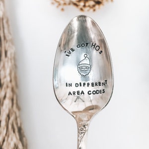 May include: A silver spoon with the text "I've got hos in different area codes" and a small illustration of Santa Claus.