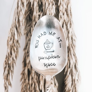 Puede incluir: Una cuchara de plata con un diseño que dice "You had me at... pumpkin spice" con un dibujo de una taza de café con crema batida en la parte superior.