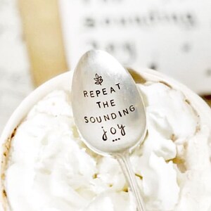 May include: A silver spoon with the words "Repeat the Sounding Joy" engraved on it. The spoon is resting in a cup of hot chocolate topped with whipped cream.