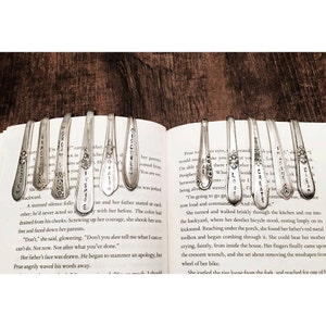 Pode incluir: Uma cole&ccedil;&atilde;o de colheres de prata com palavras como "Discover", "Love", "Create" e "Inspire" gravadas nelas. As colheres s&atilde;o usadas como marcadores de livros e s&atilde;o colocadas em um livro aberto.