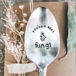 May include: A silver spoon with the text "You're a real fungi" engraved on it. The spoon has a mushroom graphic and is a fun gift for a friend who loves mushrooms.