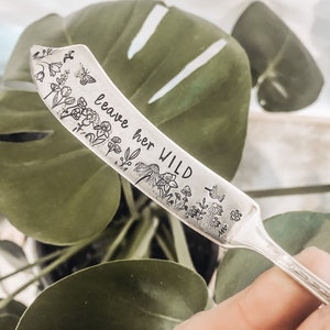 May include: A silver butter knife with a floral design and the text "leave her WILD" engraved on the blade.