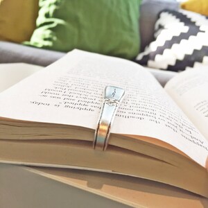 Pode incluir: Um close-up de um livro aberto com um marcador de p&aacute;gina prateado. O livro est&aacute; sobre uma superf&iacute;cie cinza. O texto na p&aacute;gina diz "And that the deadline is today."