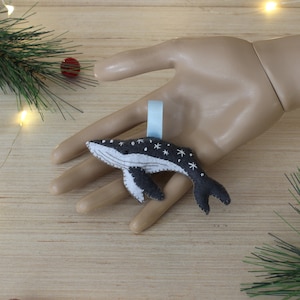 May include: A gray felt whale ornament with white snowflake details and a light blue ribbon for hanging.