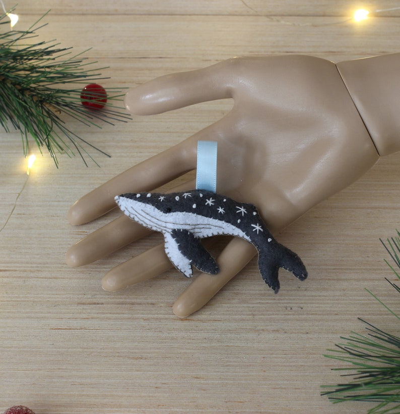 May include: A gray felt whale ornament with white snowflake details and a light blue ribbon for hanging.
