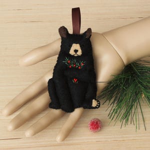May include: Black felt Christmas ornament of a bear with red berries and green leaves.