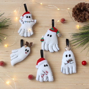 May include: Five felt ghost ornaments with different Christmas-themed details. Each ghost is white with black stitching and has a red Santa hat, a reindeer head, a green holly sprig, a silver star, or a candy cane.