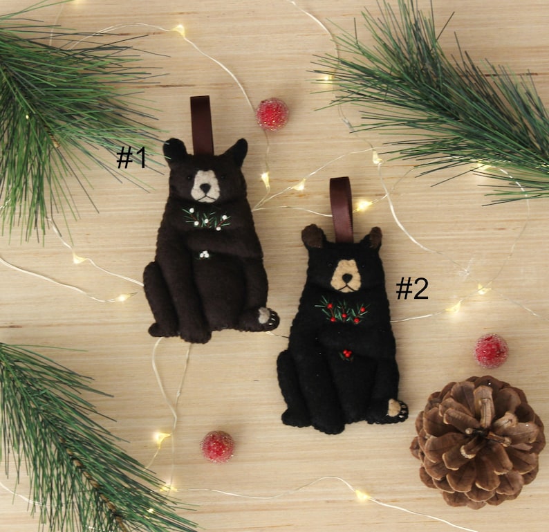 May include: Two felt black bear ornaments with red berries and green leaves. The ornaments are numbered #1 and #2.
