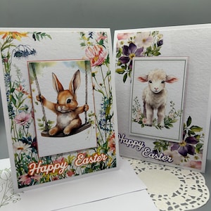 May include: Two Easter greeting cards. One card features a watercolor image of a brown bunny on a swing, the other a lamb. Both cards have floral borders and the words "Happy Easter".