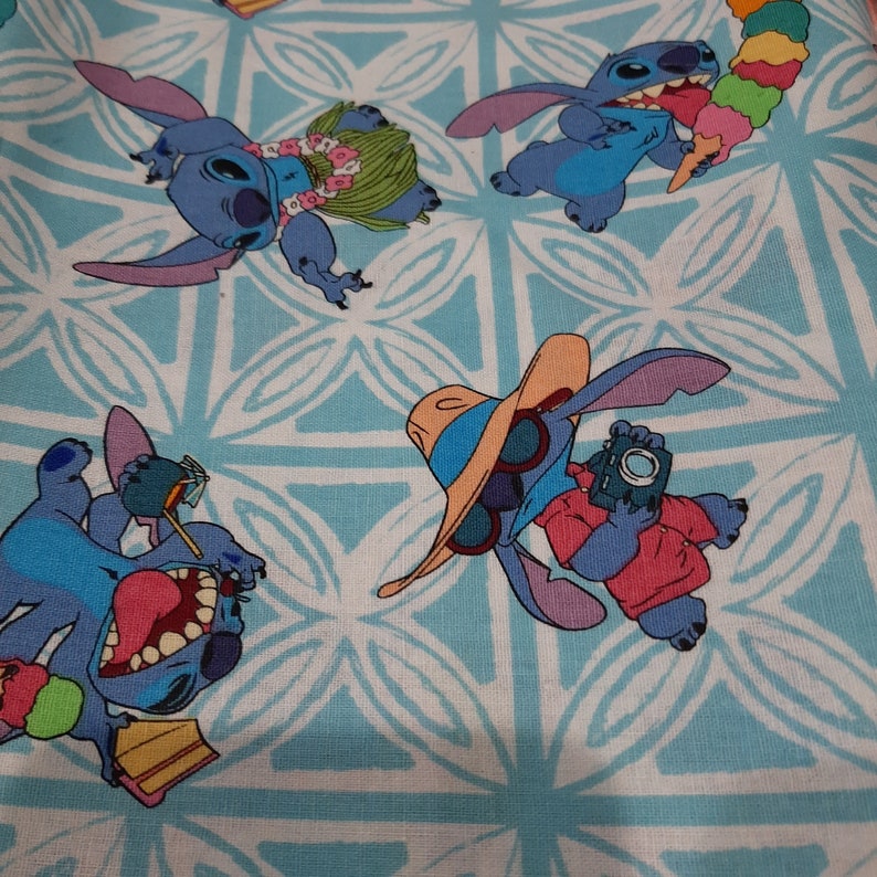 Puede incluir: Una tela azul claro con un patr&oacute;n repetido de dise&ntilde;os florales blancos y el personaje de dibujos animados Stitch en varias poses. Stitch se muestra con un lei, sosteniendo helado y tomando fotos. El tema general es tropical.