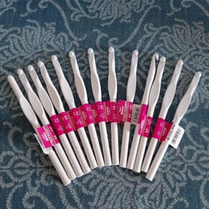 May include: A collection of white crochet hooks with pink and white labels. The hooks are arranged in a fan shape, showcasing their smooth, ergonomic design. The labels display the hook size, 8.0 mm, and the brand name, Bates.