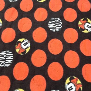 Puede incluir: Tela negra con un patr&oacute;n de grandes c&iacute;rculos naranjas y dise&ntilde;os de Minnie Mouse. Las im&aacute;genes de Minnie Mouse est&aacute;n en c&iacute;rculos amarillos con las palabras "Minnie Mouse" en un c&iacute;rculo blanco.