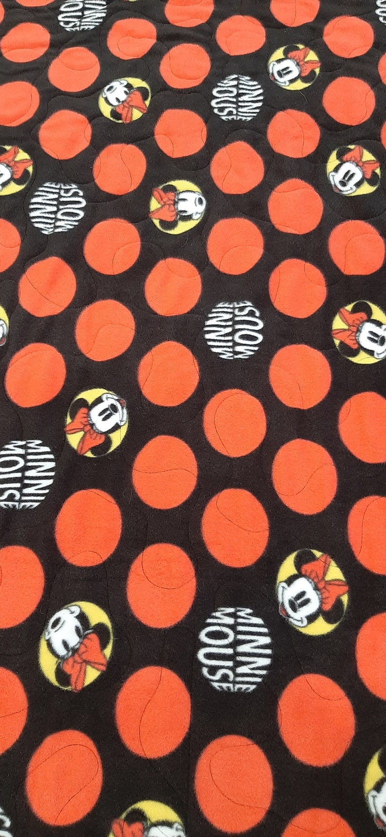 Puede incluir: Tela negra con un patr&oacute;n de grandes c&iacute;rculos naranjas y dise&ntilde;os de Minnie Mouse. Las im&aacute;genes de Minnie Mouse est&aacute;n en c&iacute;rculos amarillos con las palabras "Minnie Mouse" en un c&iacute;rculo blanco.