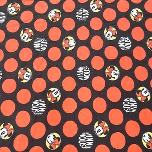 Puede incluir: Tela negra con un patr&oacute;n de grandes c&iacute;rculos naranjas y dise&ntilde;os de Minnie Mouse. Los dise&ntilde;os de Minnie Mouse est&aacute;n en c&iacute;rculos amarillos con las palabras "MINNIE MOUSE" en blanco.