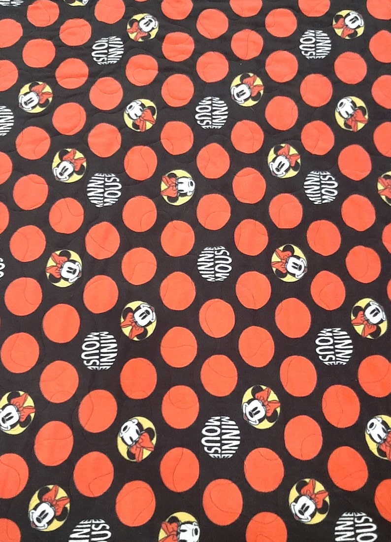 Puede incluir: Tela negra con un patr&oacute;n de grandes c&iacute;rculos naranjas y dise&ntilde;os de Minnie Mouse. Los dise&ntilde;os de Minnie Mouse est&aacute;n en c&iacute;rculos amarillos con las palabras "MINNIE MOUSE" en blanco.