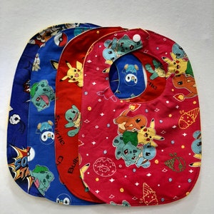May include: Four colorful baby bibs with a Pokemon theme. The bibs are red, blue, yellow, and green with various Pokemon characters printed on them. The bibs have a yellow trim around the edges.