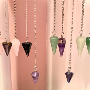 May include: A set of 10 crystal pendulums with silver chains. The crystals are in various colours, including pink, green, black, purple, and brown.
