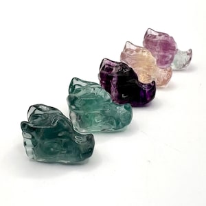 May include: Five carved crystal dragon figurines in shades of green, purple, and pink. The dragons are arranged in a row, each with detailed features. The translucent stones catch the light, showcasing the intricate carvings. These decorative figurines are ideal for collectors.