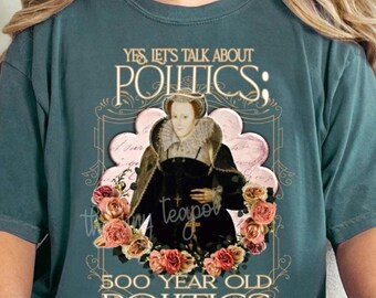 May include: A teal blue t-shirt with a vintage-style illustration of a woman in a crown and a quote that reads "Yes let's talk about politics; 500 year old politics".