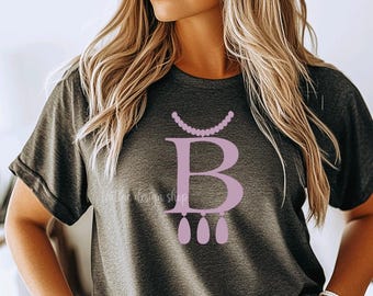 May include: A dark gray t-shirt with a pink letter "B" and a pink pearl necklace design. The necklace is attached to the top of the letter "B" and has three pink teardrop-shaped pendants hanging from the bottom.