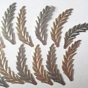 May include: Twelve gold-toned metal leaf sprigs with a textured finish. The sprigs are arranged in a random pattern on a white background.