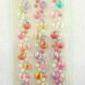 May include: A sheet of iridescent, multi-colored, round, self-adhesive gems. The gems are arranged in vertical rows, with each row featuring a different color. The colors include pink, purple, blue, green, and yellow.