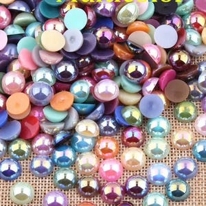 May include: A large collection of small, round, flat-backed cabochons in a variety of colors including pink, blue, purple, orange, and green. Many of these pieces feature a glossy, iridescent finish that reflects light, creating a shimmering effect.