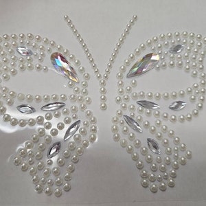 May include: A white butterfly-shaped design made of small white pearls and iridescent rhinestones.