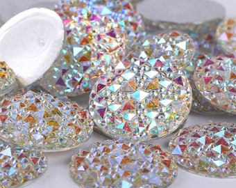 May include: A group of iridescent round rhinestones with a faceted design. The rhinestones are clear with a rainbow effect.