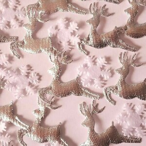 Puede incluir: Una colección de adornos de reno plateados con adornos de copo de nieve rosa. Los renos están en una variedad de poses, algunos con la cabeza levantada y otros con la cabeza baja. Los copos de nieve están dispersos alrededor de los renos.