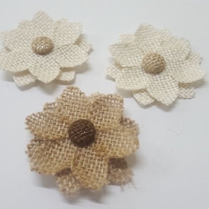 Puede incluir: Tres flores de arpillera con centros marrones. Las flores son blancas y marrones.