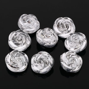 May include: Eight clear plastic rose-shaped buttons. The buttons are about 1 inch in diameter and have a raised, three-dimensional design.