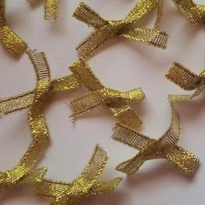 May include: A collection of small, gold mesh bows scattered on a white surface. The bows are intricately woven, with a shimmering, metallic appearance. These decorative bows are suitable for various craft projects and gift wrapping.