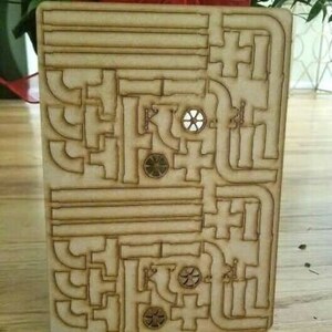 May include: A wooden maze with a laser-cut design. The maze has a series of interconnected paths and circles. The maze is made of light brown wood.