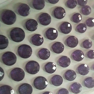 May include: A sheet of purple, round, self-adhesive gems. The gems have a faceted, sparkly finish.