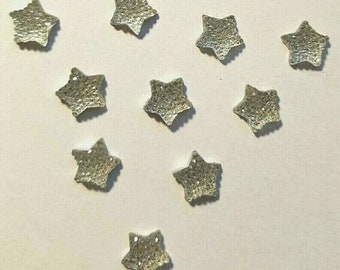 May include: Ten silver glitter star-shaped embellishments. The stars are approximately 1 inch in diameter.