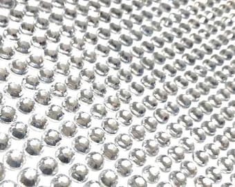 May include: A sheet of clear, round, self-adhesive rhinestones. The rhinestones are arranged in a grid pattern.