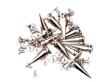 May include: A pile of silver metal cone studs with pointed ends and screw fixings. The studs are scattered on a white background, with several small screws and washers also visible.