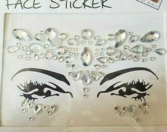 May include: A sheet of face stickers with a design of rhinestones arranged around two eyes. The rhinestones are clear and have a variety of shapes and sizes.