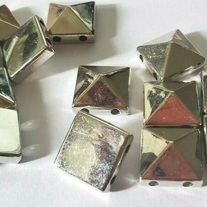 May include: A group of silver pyramid-shaped studs with a square base. The studs have two holes on each side.