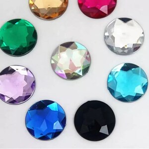 May include: Assortment of ten round, faceted, glass rhinestones in various colours, including clear, black, green, blue, purple, turquoise, and iridescent.