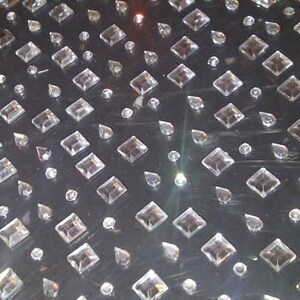 May include: A close-up of a silver surface covered in clear, faceted rhinestones of various sizes and shapes. The rhinestones are arranged in a repeating pattern.