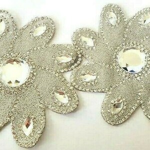 May include: Two silver sparkly flower-shaped embellishments with clear rhinestones in the center. The embellishments are perfect for adding a touch of sparkle to crafts, clothing, or home decor.