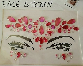May include: A sheet of face stickers with pink and clear rhinestones in a variety of shapes and sizes. The stickers are arranged in a design that includes two eyes. The sheet is labeled "FACE STICKER".