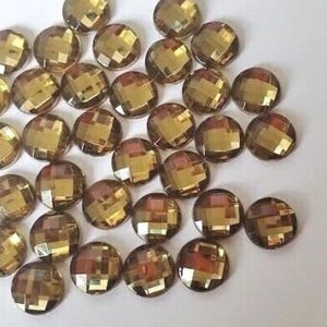 以下が含まれることがあります： 丸いファセットカットの金色ガラスラインストーンのコレクション。ラインストーンは白い表面に散らばっています。