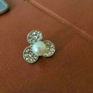 May include: A silver flower-shaped brooch with a pearl in the centre and rhinestones around the edges.