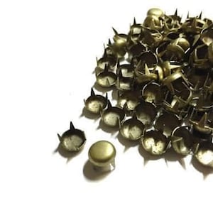 May include: A large pile of antique gold-toned metal studs with four prongs. The studs are scattered on a white surface.