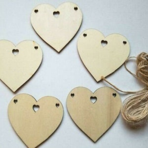 Puede incluir: Cinco adornos de madera en forma de corazón sin terminar con pequeños recortes en forma de corazón. Los corazones están ensartados con un cordel.